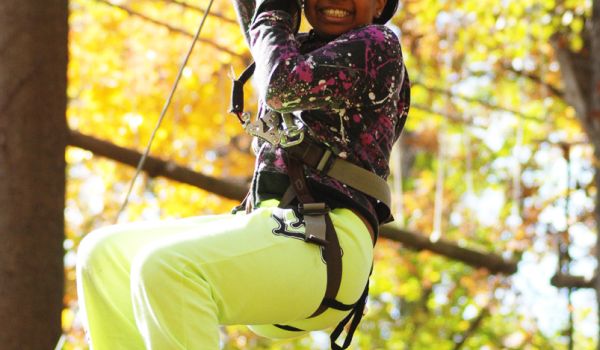 A young girl holding on tight and smiling as she rides the zip line at the aerial adventure park at Catamount Resort
