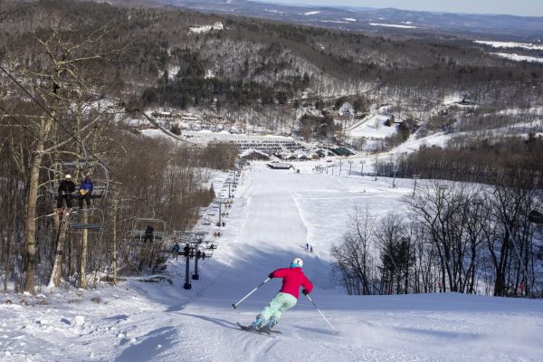 A woman skiing down to the lodge on a sunny day. Click here for hours of operations at Catamount Resort.