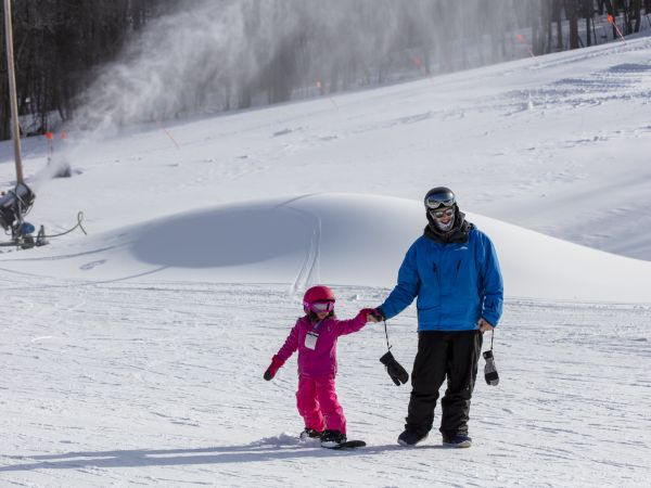 A snowboard instructor assisting a little girl in a lesson.