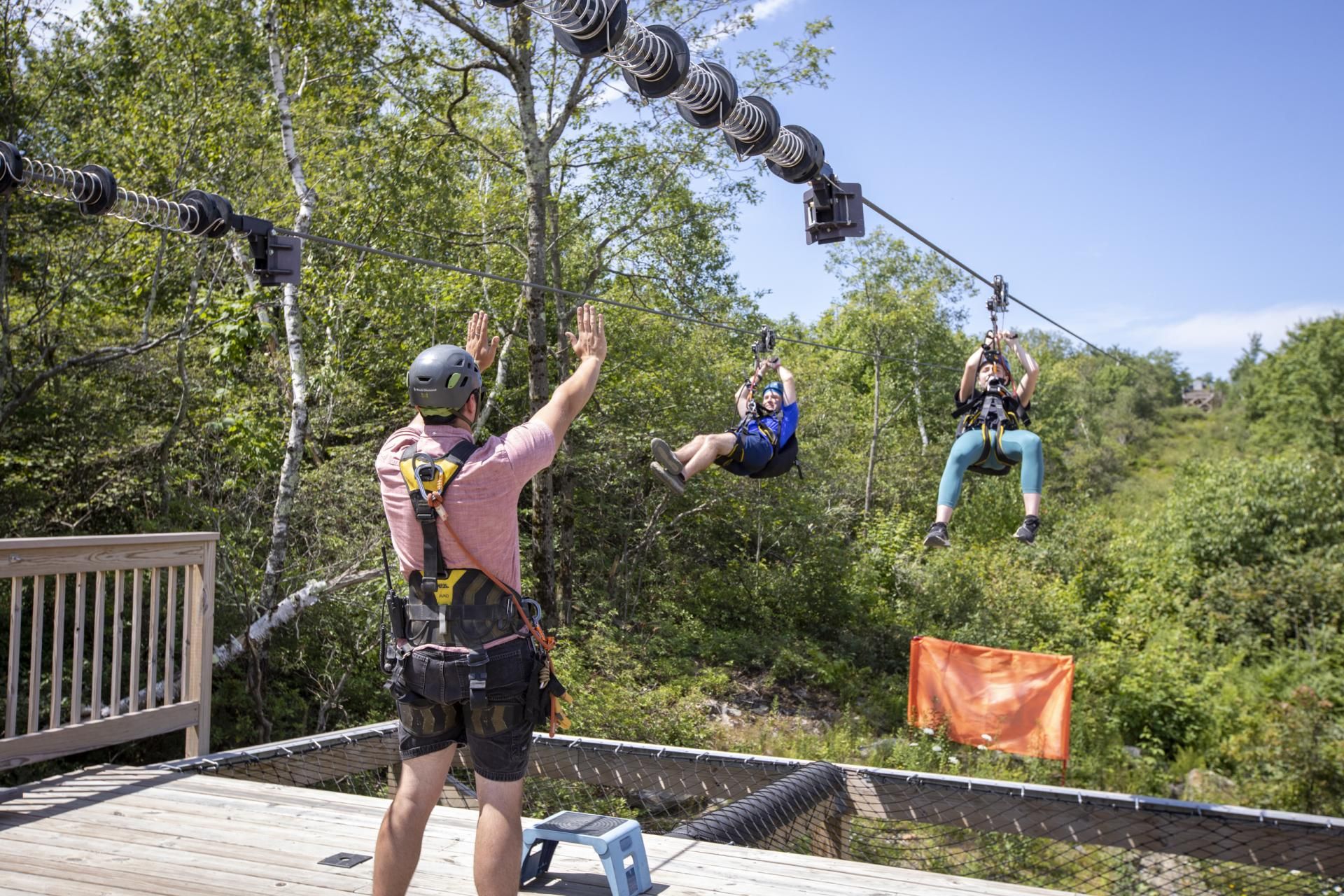 Zip Tour Guide standing at bottom of zipline with two zipliners riding down.