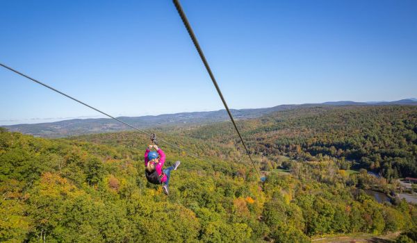 A woman going down the zipline with a magnificent view of the valley below at Catamount Resort