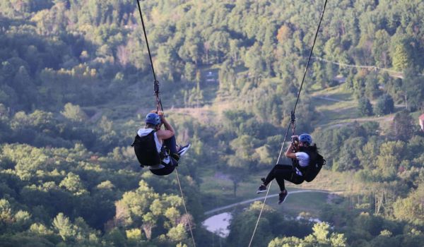 Two people high above the valley on the Catamount Zipline